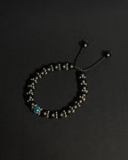 A beaded adjustable bracelet with matte black onyx beads, small metallic spacer beads, and a single blue apatite bead, displayed on a dark background.