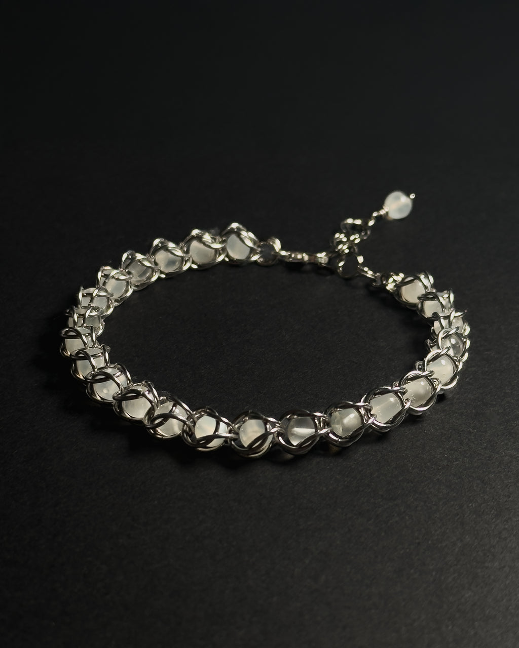 A silver-toned beaded bracelet with faceted clear stones, displayed on a dark black background.