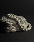 A silver-toned capture bead bracelet with natural white moonstone gemstones draped over a textured gray rock against a solid black background.