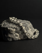 A silver-toned capture bead bracelet with natural white moonstone gemstones draped over a textured gray rock against a solid black background.