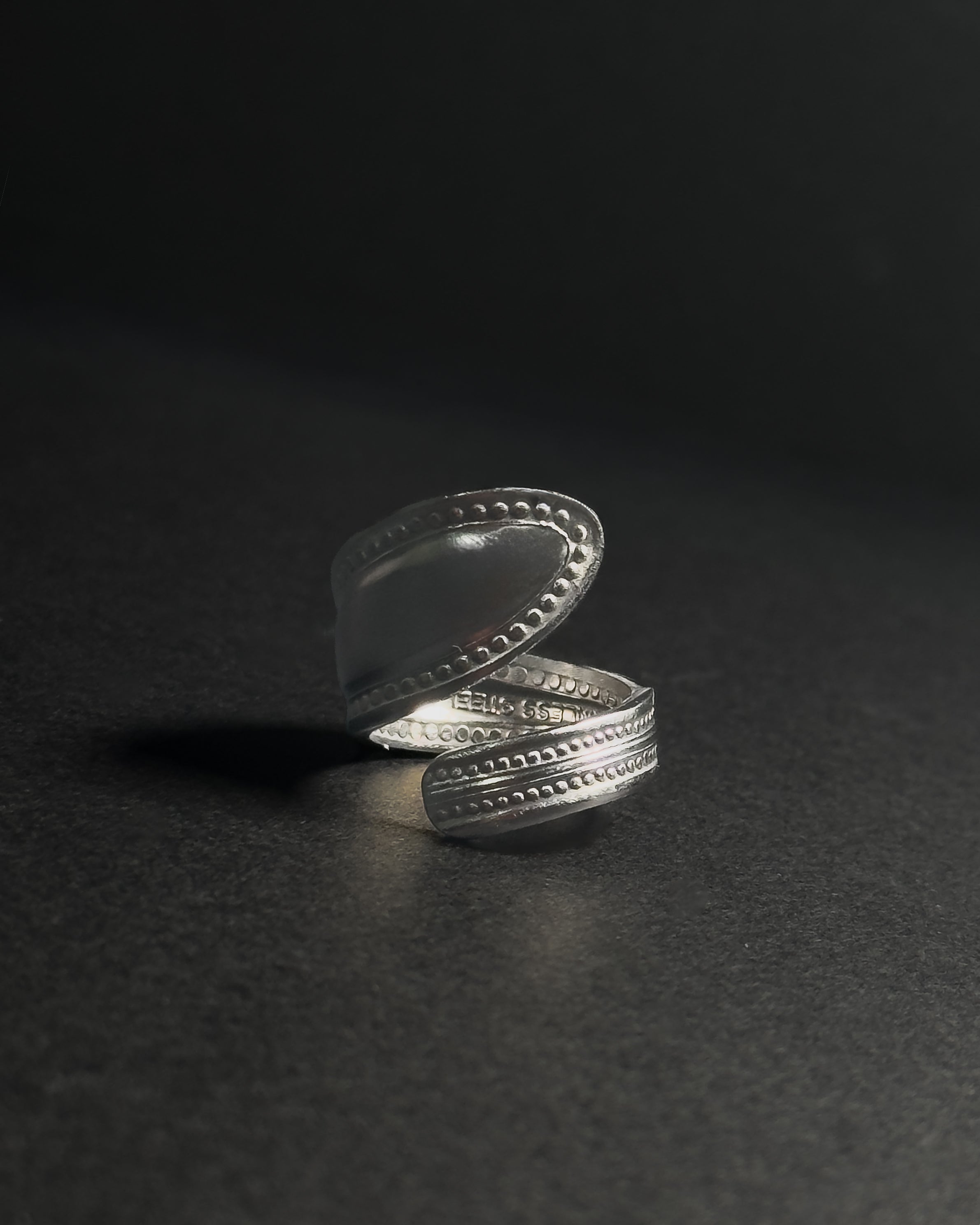 Solid stainless steel spoon ring with a textured, stud-like in a wrap finish, shown open on a dark surface.