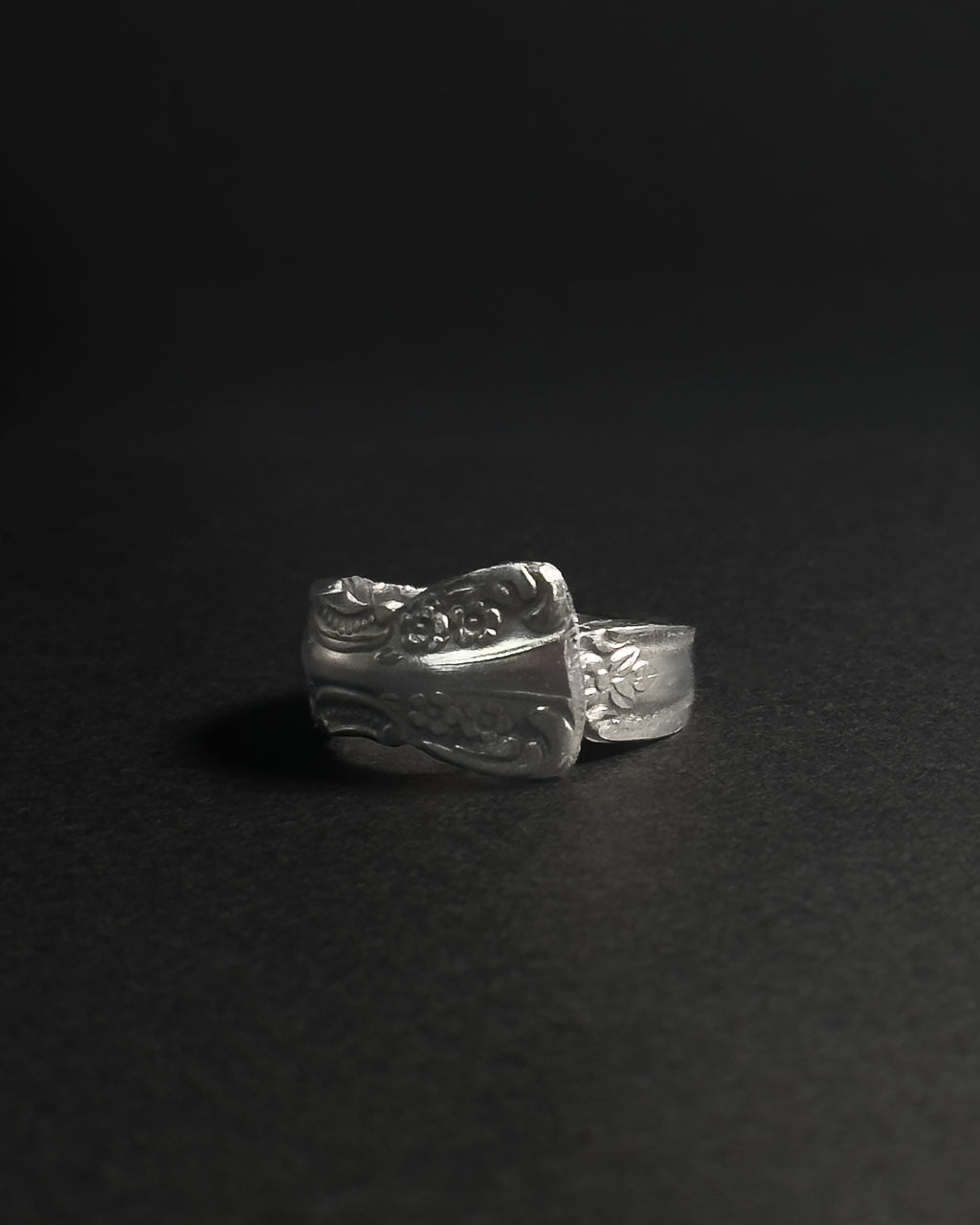 Solid stainless steel spoon ring handcrafted from vintage silverware patterns in a fixed size, displayed on a dark black background.