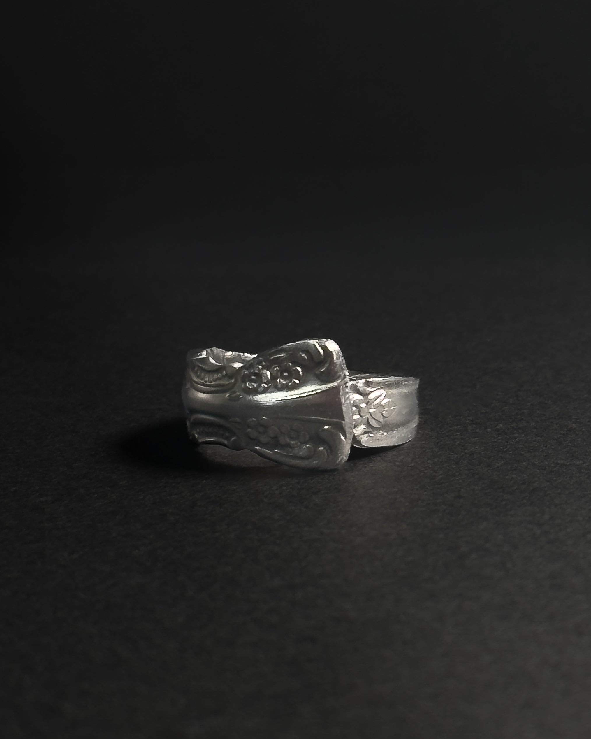 Solid stainless steel spoon ring handcrafted from vintage silverware patterns in a fixed size, displayed on a dark black background.