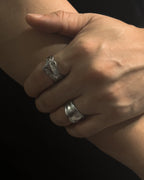 A close-up of a person's hand and forearm wearing two Solid stainless steel spoon ring handcrafted from vintage silverware patterns in a fixed size against a black background.