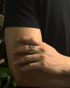 A close-up of a person's hand resting on their arm, wearing a Solid stainless steel spoon ring in black t-shirt and leafy background