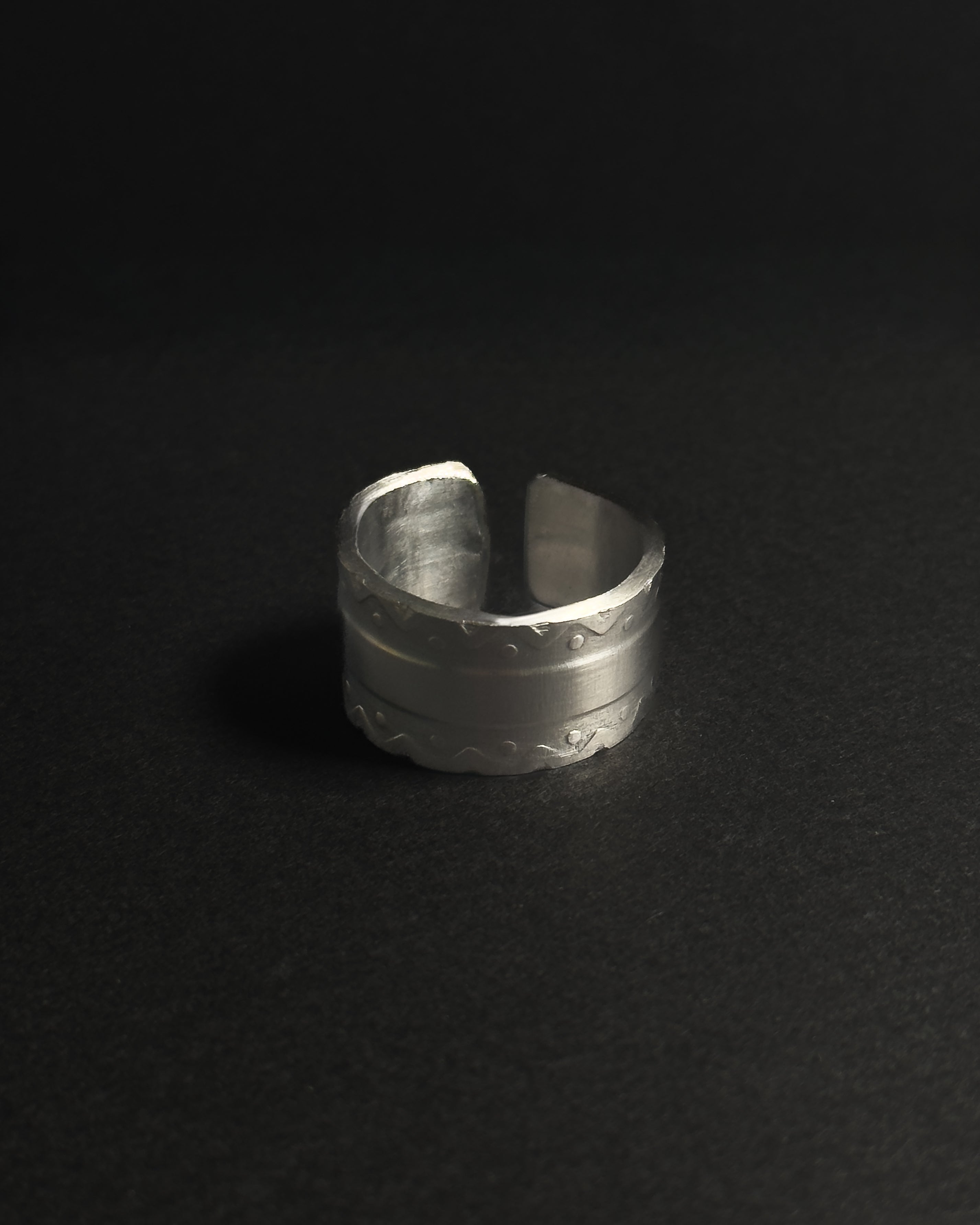 Solid stainless steel spoon ring displayed on a dark, matte black surface.