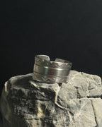 Solid stainless steel spoon ring cuff ring with engraved wavy patterns, displayed on a textured gray rock against a dark black background.