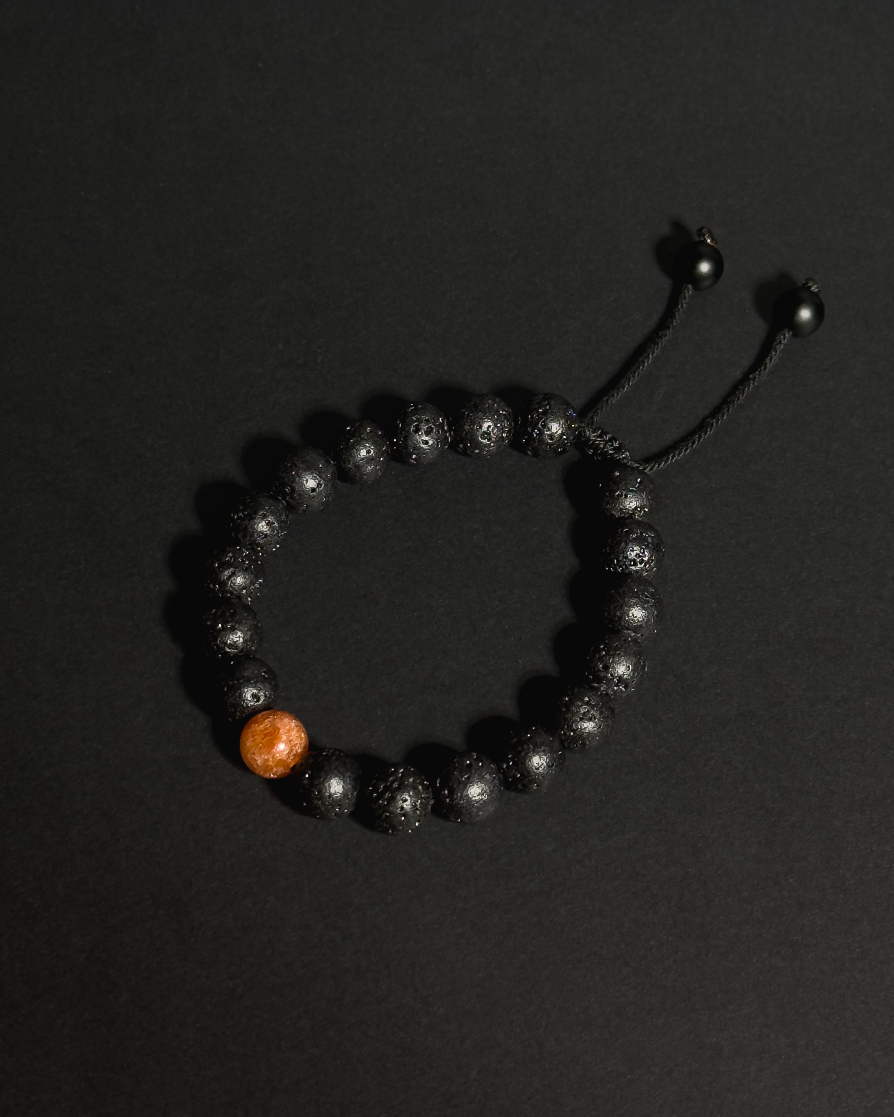 Close-up of natural 10mm sunstone and lava stone beads on The Rising Sun Bracelet showing unique stone textures and variations.