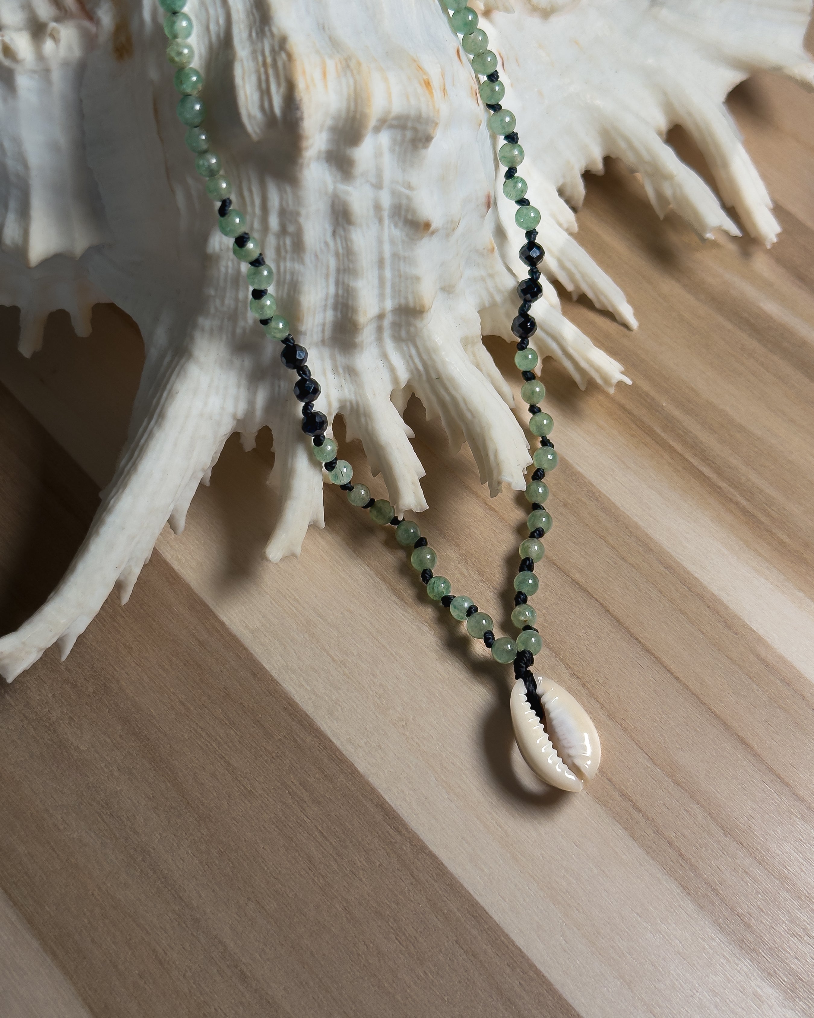 Beaded Necklace with green beads and a shell pendant on a wooden surface with a large shell in the background.