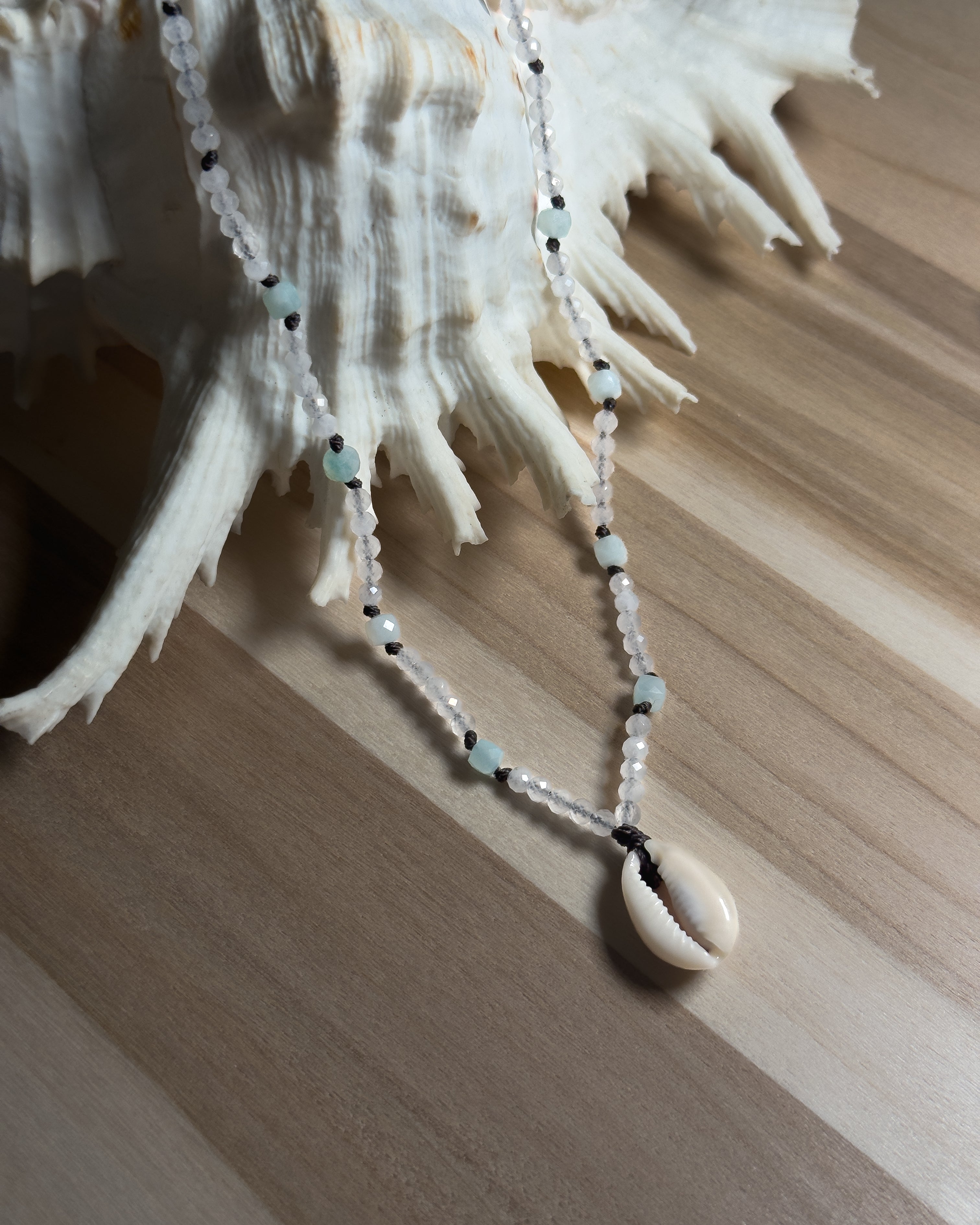 Beaded Necklace with shell pendant on a seashell against a wooden background