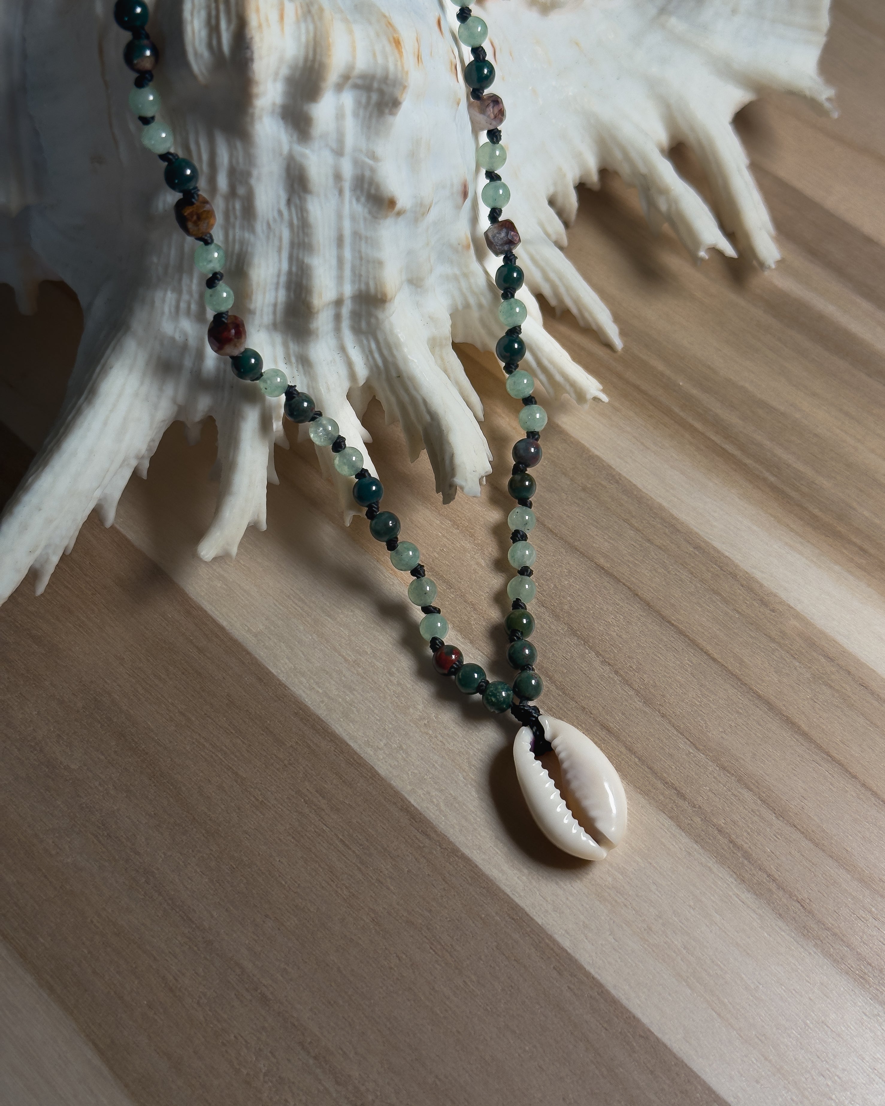 Necklace with beads and a shell pendant on a seashell against a wooden background