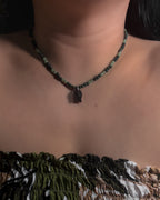 Necklace with dark green beads with black faceted crystal fish pendant worn by a model against a neutral background