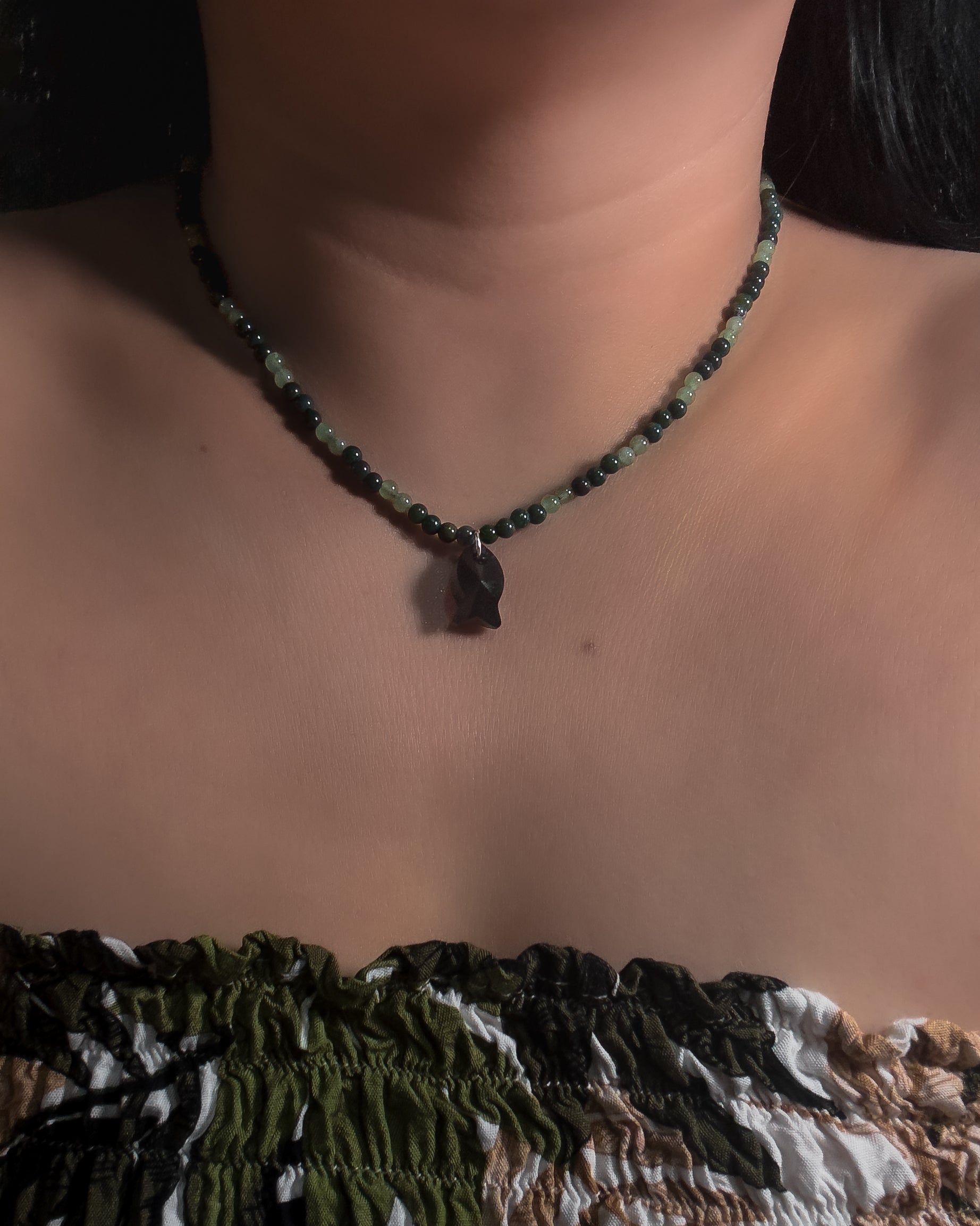 Necklace with dark green beads with black faceted crystal fish pendant worn by a model against a neutral background