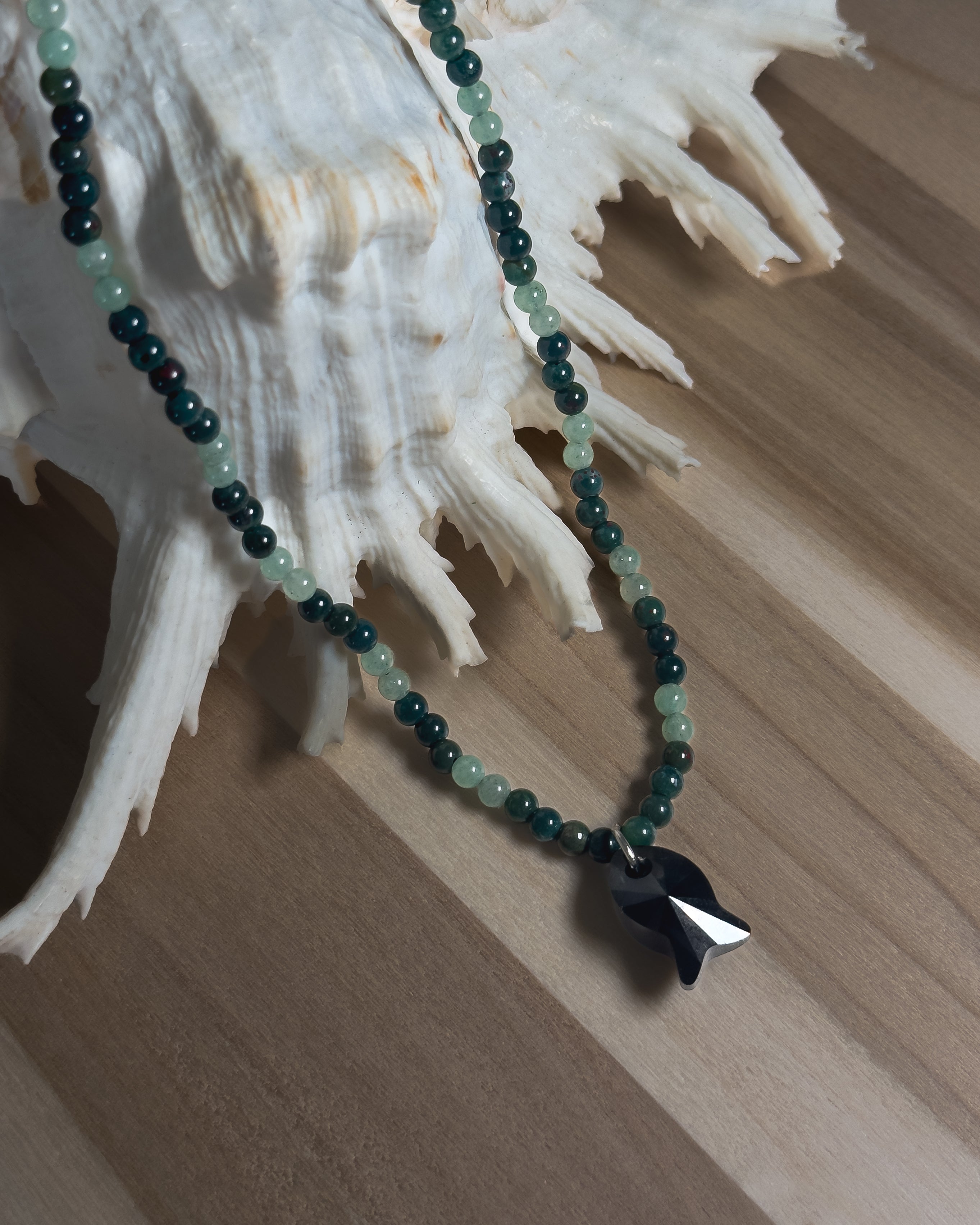 Necklace with green beads and a black faceted crystal fish pendant on a shell background
