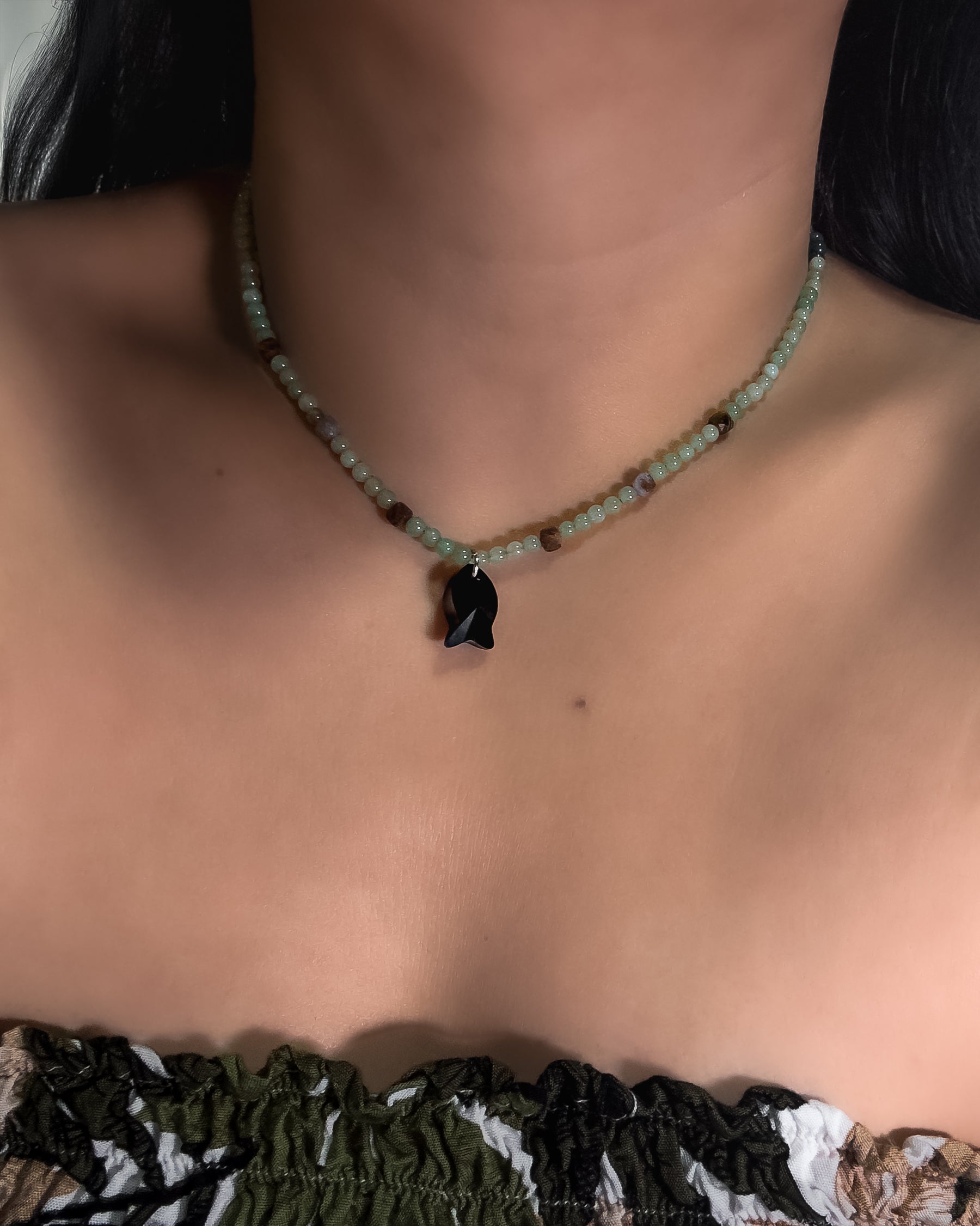 Necklace with a black faceted crystal fish pendant on a person wearing a green top.