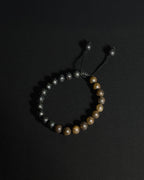 A beaded bracelet featuring natural  lava stone and bronzite , with a black adjustable cord closure, displayed on a dark background.