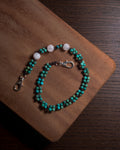 A beaded phone charm keychain with turquoise-blue and white beads, with silver toned stainless steel clasp displayed on a wooden board over a dark wood surface.