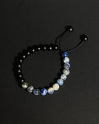 A beaded bracelet with matte black beads on one side and a section of blue, white, and gray sodalite beads on the other, connected by a black adjustable cord with black beads.