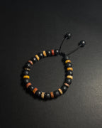 A beaded bracelet with black lava stones, yellow and brown picasso jasper accent beads, and a black adjustable cord closure, displayed on a dark background.